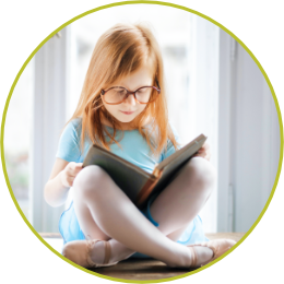 photo of a girl with glasses sitting in front of a window reading a book